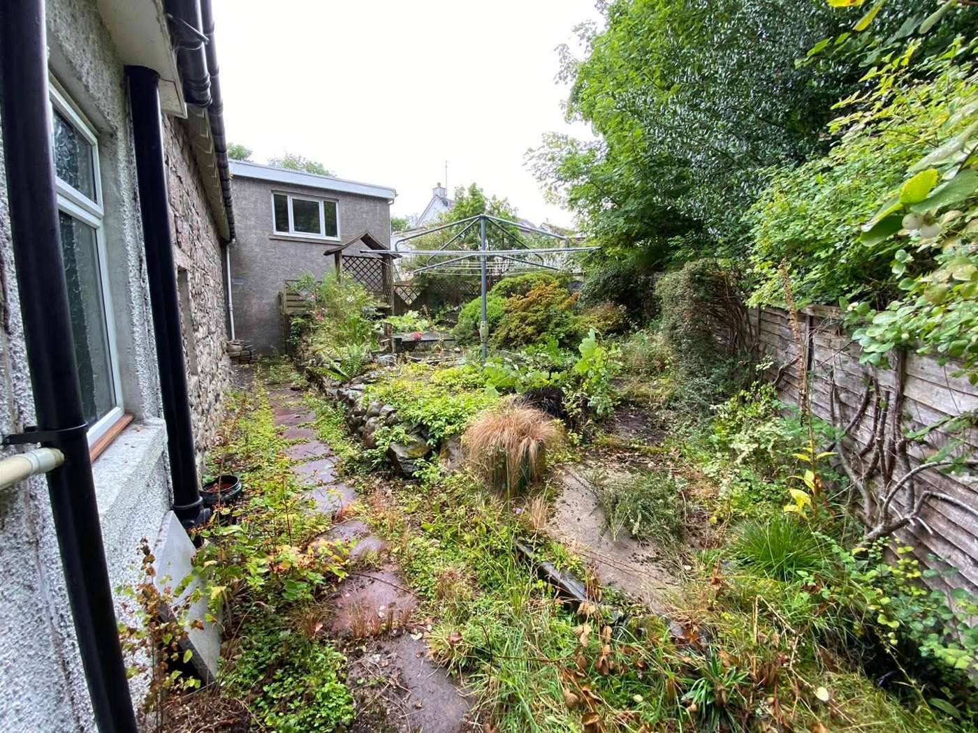 Overgrown side passage beside a stone house