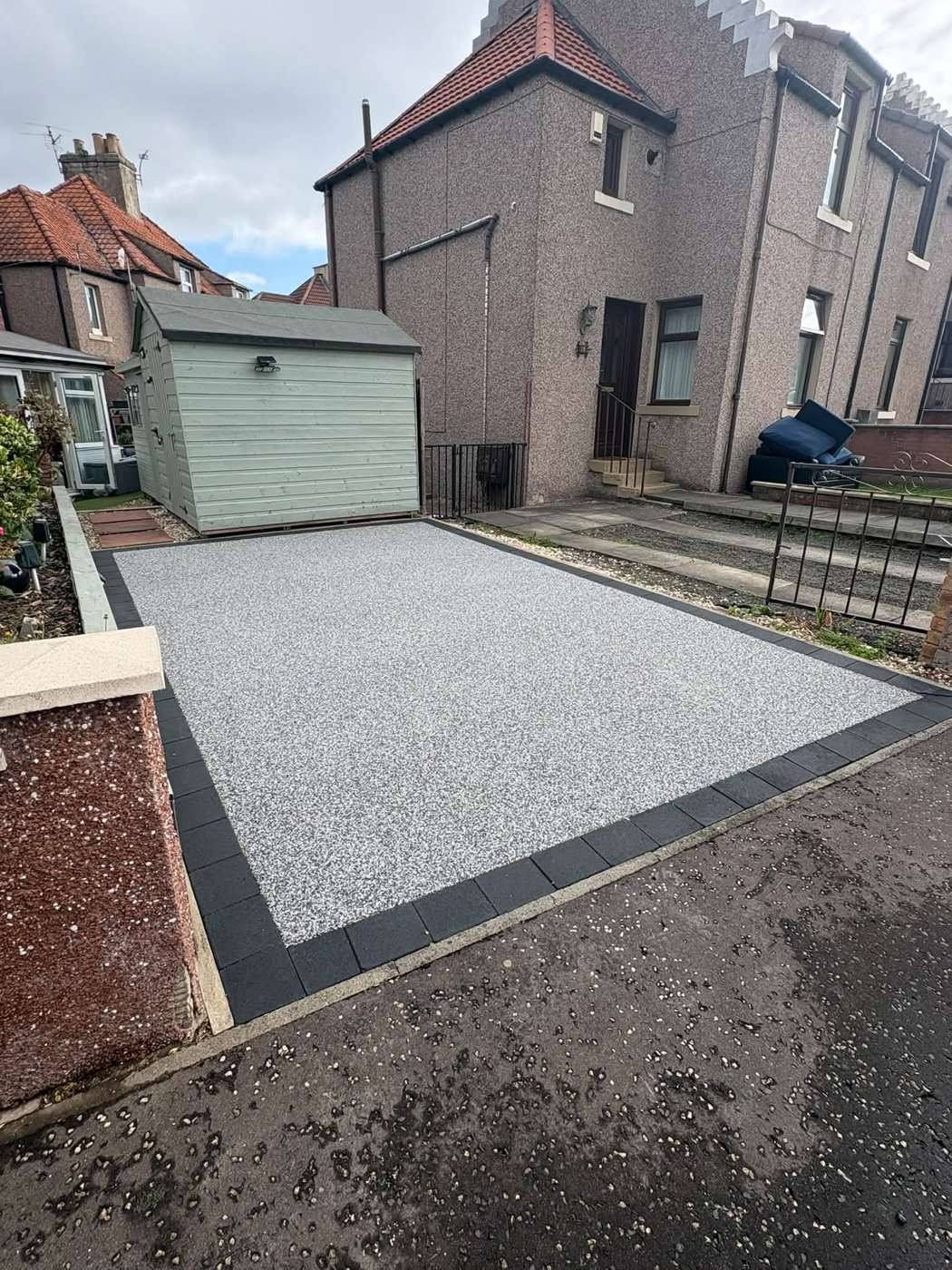 Silver resin driveway with a black border in front of the same shed