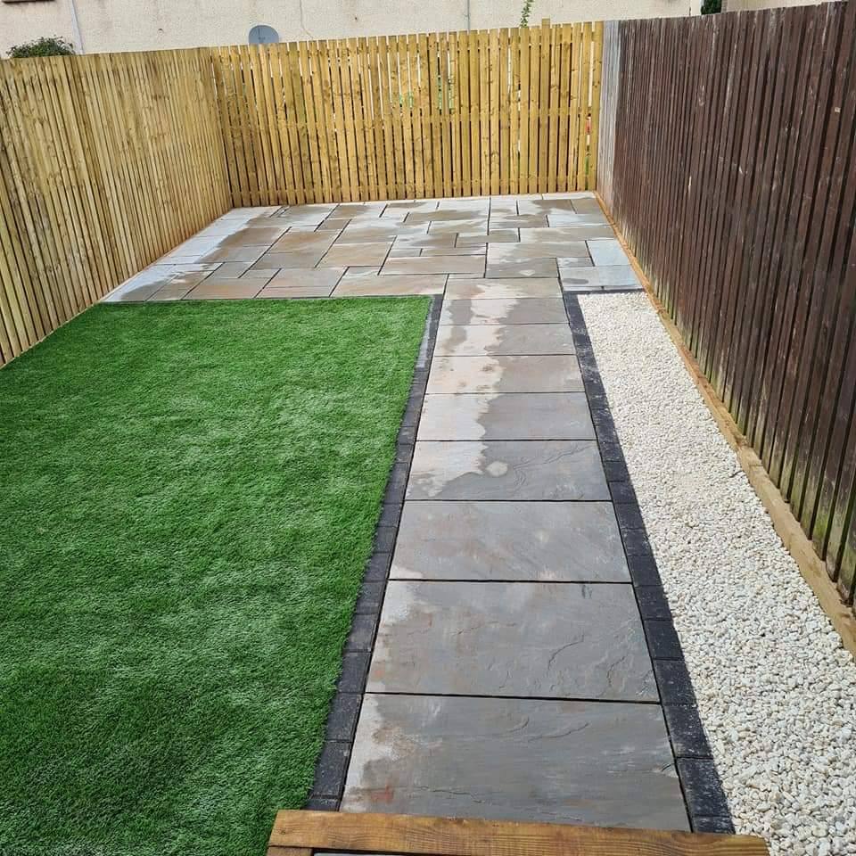Artificial grass, a paved path and white gravel between two fences