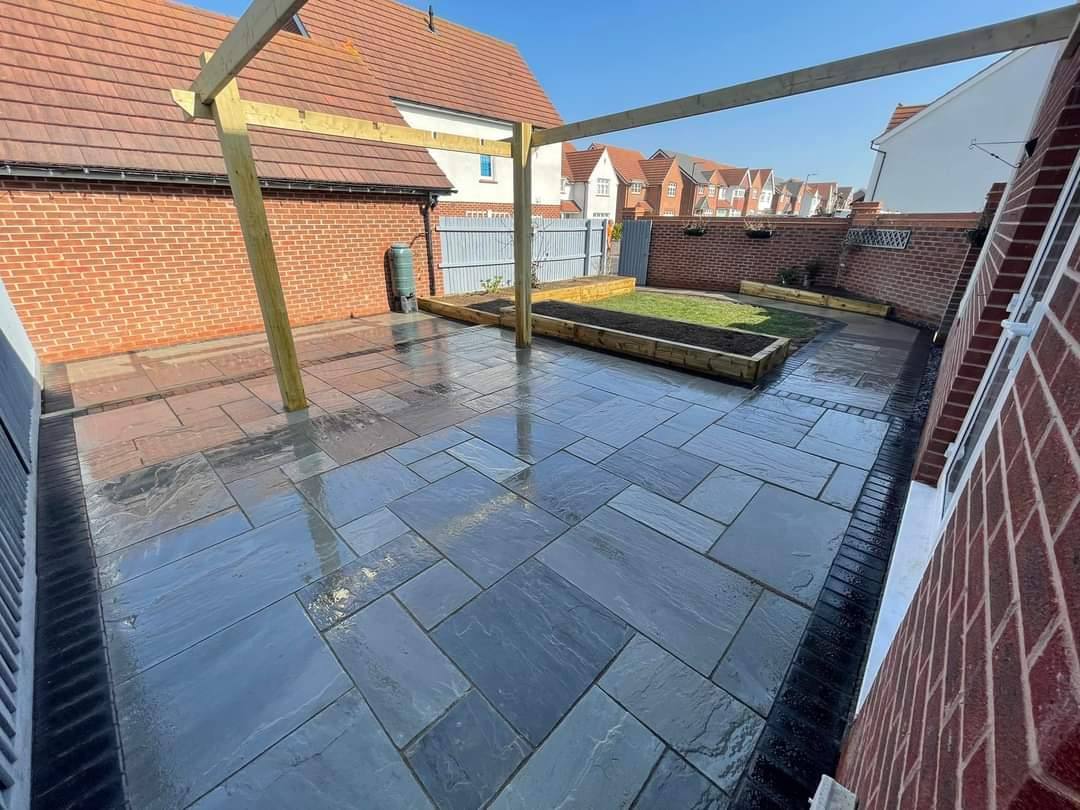 Dark porcelain patio under the same pergola, with a raised bed