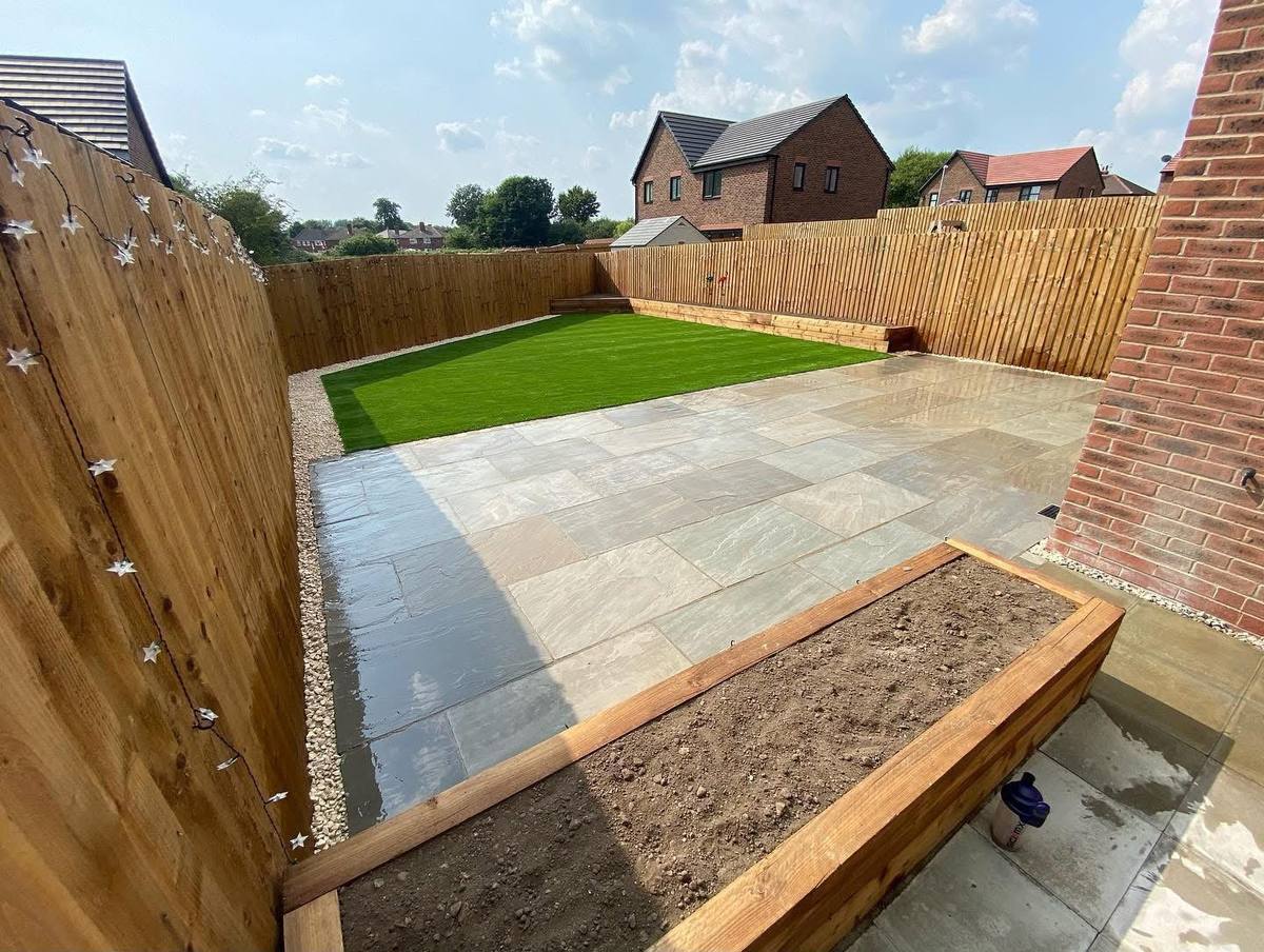 Artificial grass, sandstone patio and a planted sleeper bed in the same garden