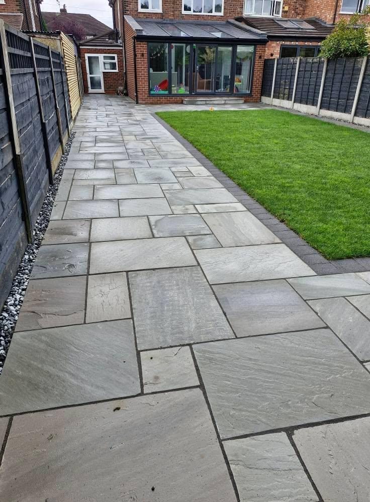 Grey porcelain path beside a lawn and dark fence