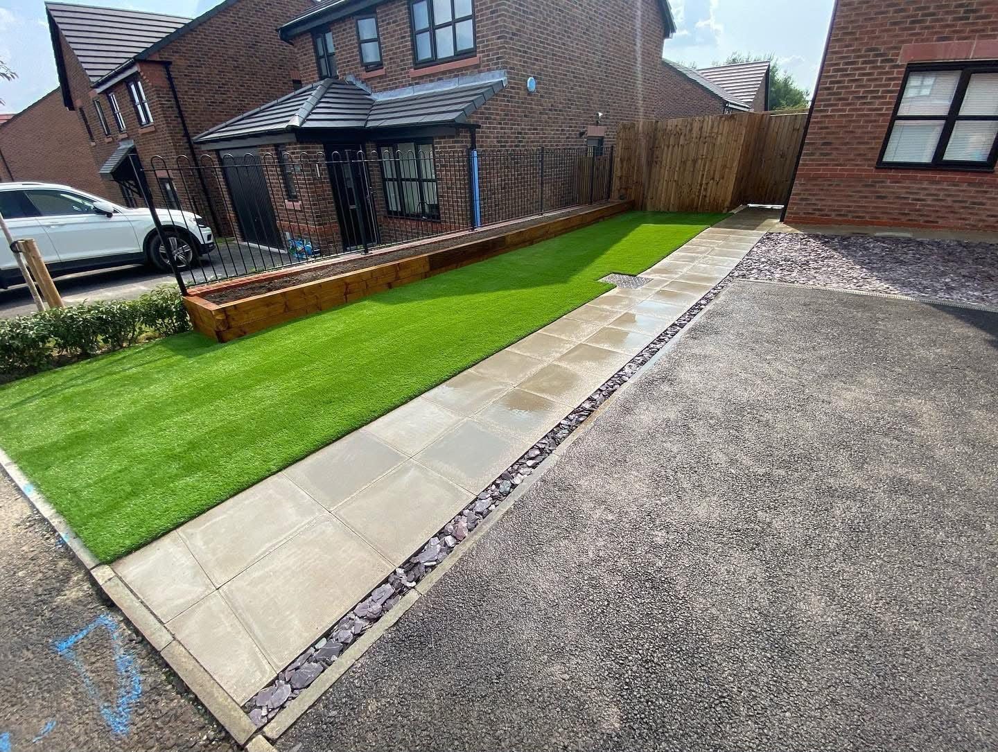 Artificial grass strip beside a new brick house and a paved path